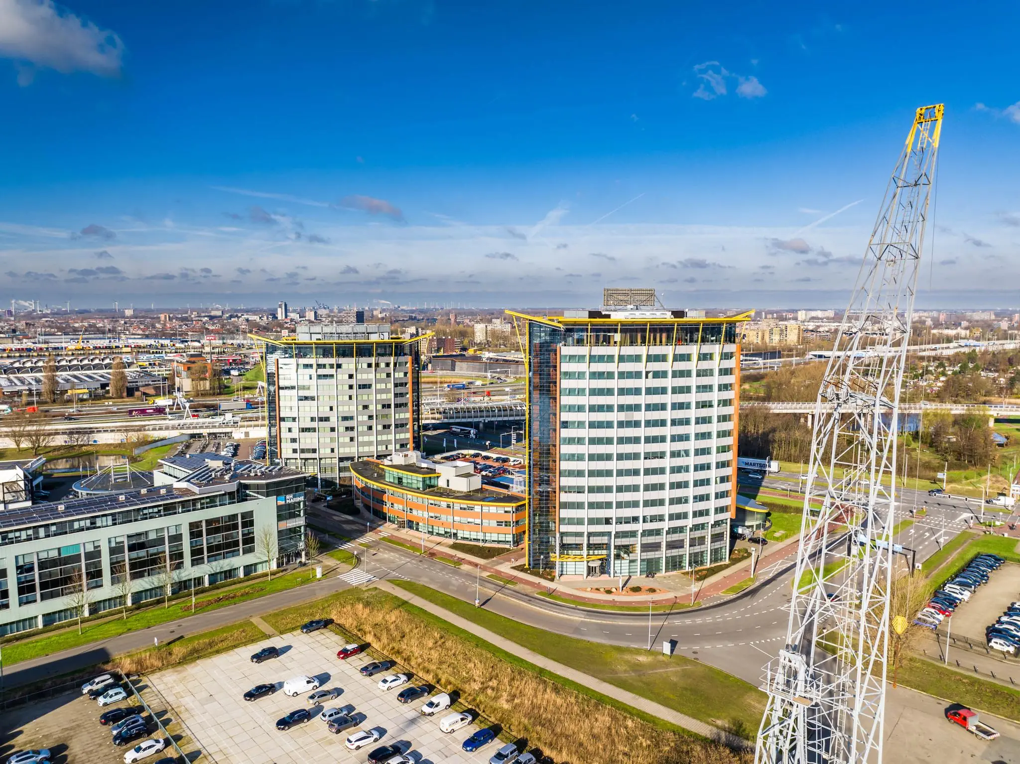 Luchtfoto van moderne kantoorgebouwen aan de Karel Doormanweg in Vlaardingen, met parkeergelegenheid en een opvallende witte kraanconstructie op de voorgrond.